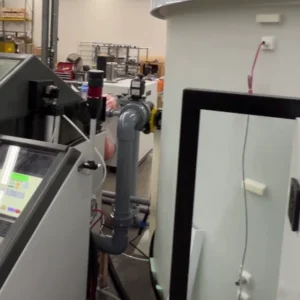 Front view of a cyclic corrosion chamber showing the digital computer control interface alongside a large white immersion solution tank in an industrial laboratory.