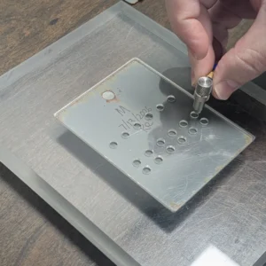 Ultrasonic thickness gauge probe measuring a Ford corrosion gauge loss verification panel through a measurement template.